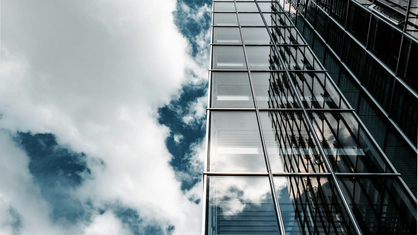 Glass office towers reflecting clouds against a blue sky.